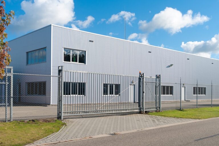 modern exterior of an industrial building, surrounded by a fence with iron gate