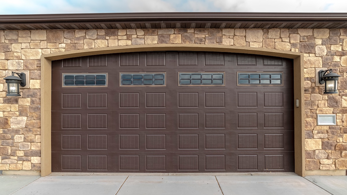 Panorama frame Large garage with double brown wooden door and decorative face brick walls with cement paved forecourt